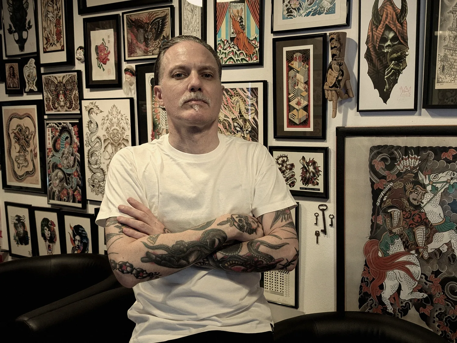 Leonel «Leo» Martínez de brazos cruzados en A Sailor's Grave Tattoo, su estudio privado en Granollers (Barcelona), delante de la pared de láminas enmarcadas del estudio.