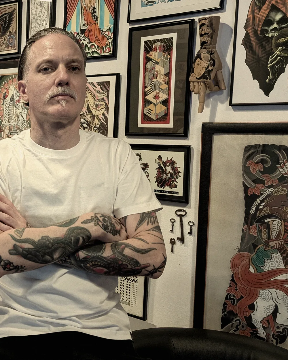 Leo Martínez sentado en la sala de A Sailor's Grave Tattoo, en Granollers, con la pared de láminas enmarcadas al fondo.